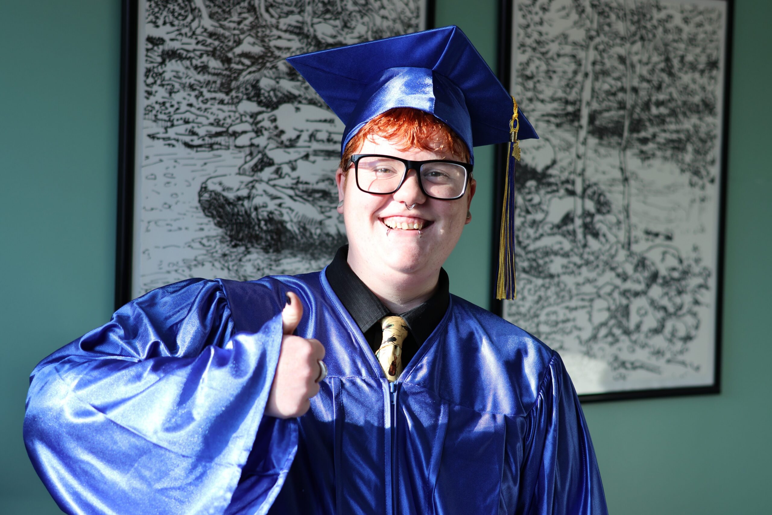 Wren wearing their cap and gown and giving a thumbs up
